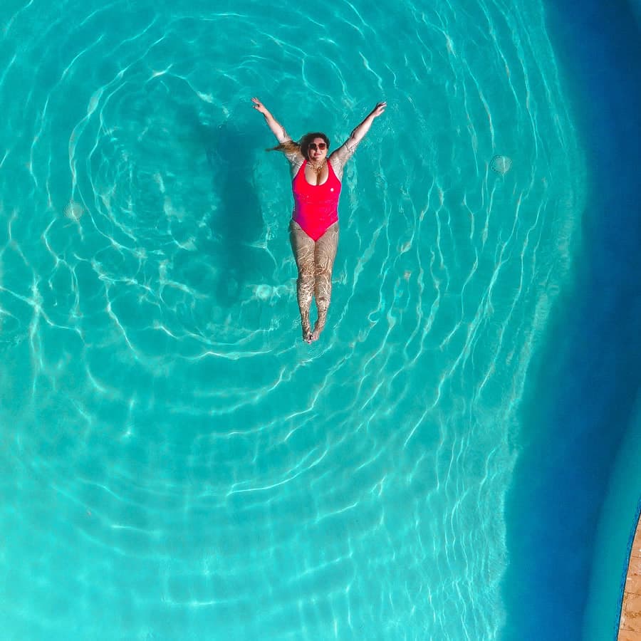 Woman in pink on piece suite - floating on back in pool.