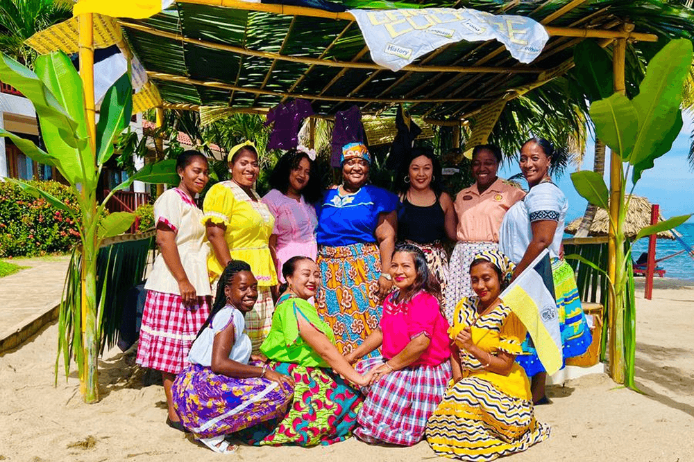 Group of Belizean woman in colorful outfits holding flags