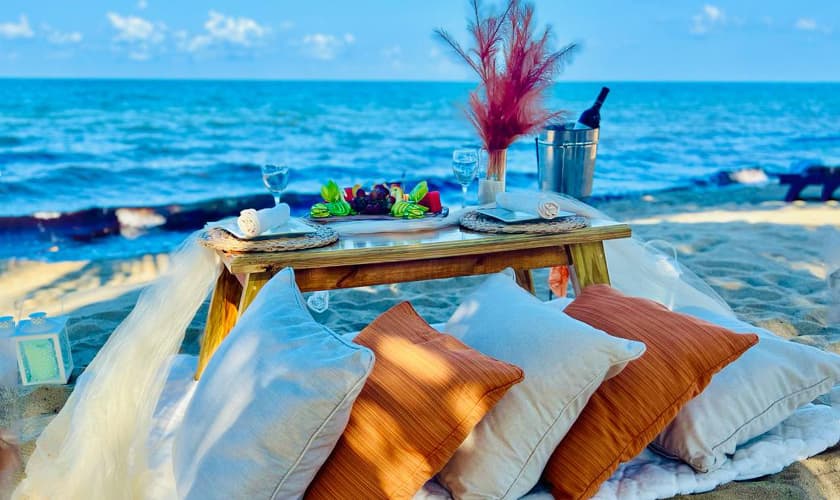 A romantic beachside picnic setup with a wooden table, decorative pillows, and fresh seafood, overlooking the ocean.