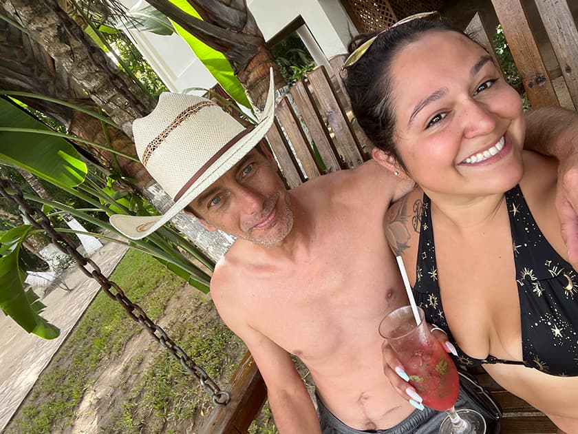 A man in a cowboy hat and a woman in a bikini smile together while sitting on a swing.