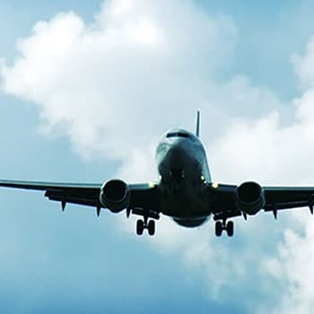 A large commercial airplane flies through the cloudy sky.