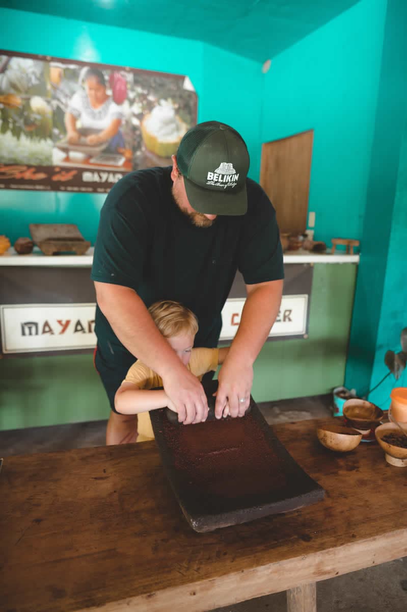 A man and a child work together on a grinding stone while surrounded by colorful walls and various bowls.