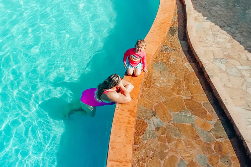 A woman relaxes in a swimming pool while a child sits on the edge nearby.