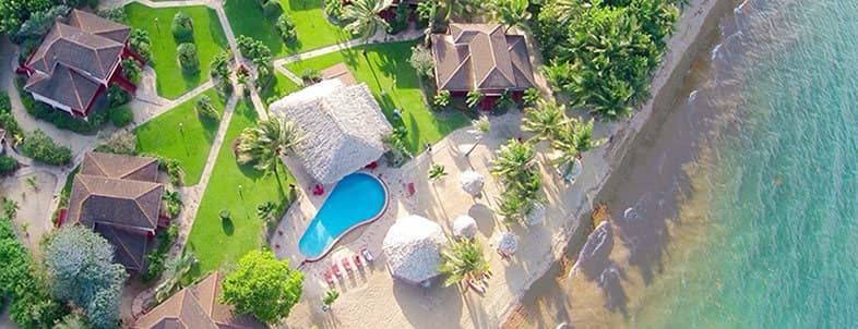 Aerial view of a tropical resort with bungalows, a pool, and a sandy beach. Aerial view of a tropical resort with bungalows, a pool, and a sandy beach.