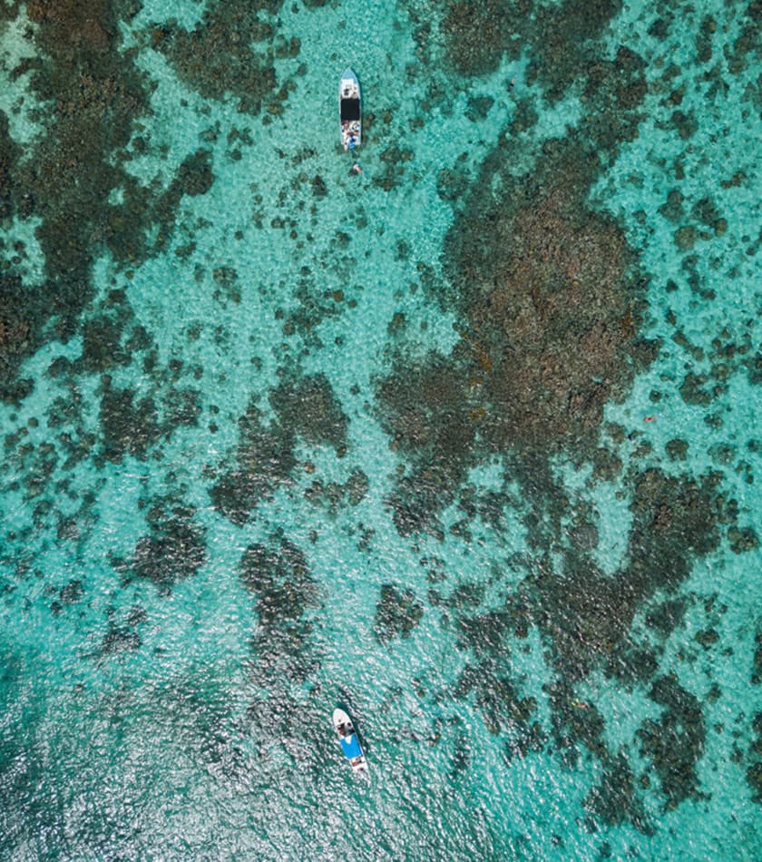 Aerial view of two boats on clear turquoise water with visible coral formations below.