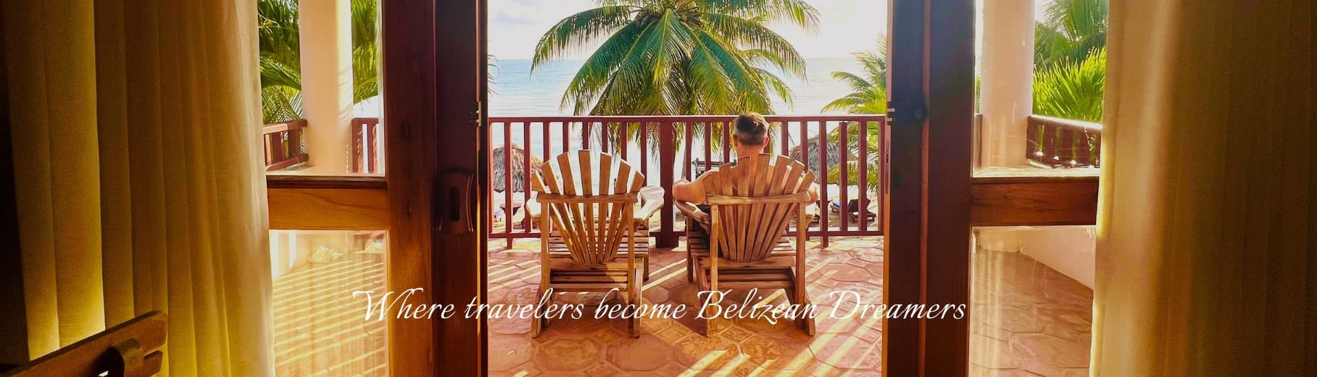 A person relaxes on a balcony with wooden Adirondack chairs, overlooking a tropical landscape.