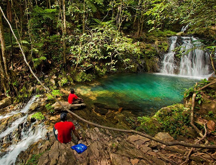 Travelers beside a rainforest waterfall pool