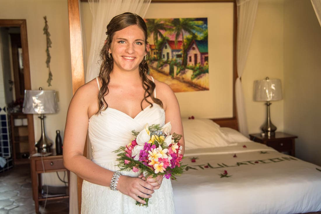 A pretty young brunette bride holding a bouquet in a guest room before her wedding.