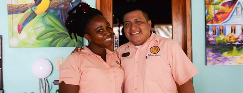 Two smiling staff members pose together in a colorful, tropical-themed setting. Two smiling staff members pose together in a colorful, tropical-themed setting.