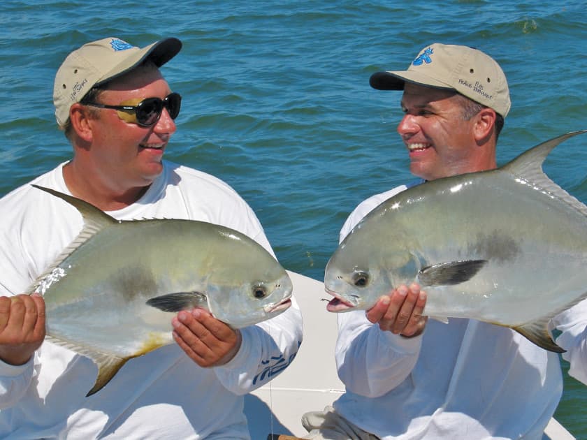 Two men holding large fish and smiling at each other on a boat. Two men holding large fish and smiling at each other on a boat.