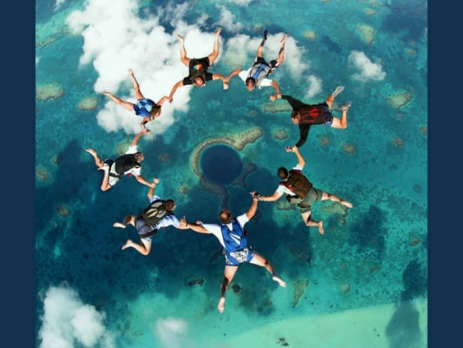 Aerial view of a group of skydivers forming a circle above a blue lagoon.