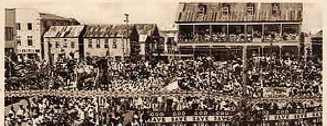 A large crowd gathers in front of historical buildings during a festive event. A large crowd gathers in front of historical buildings during a festive event.