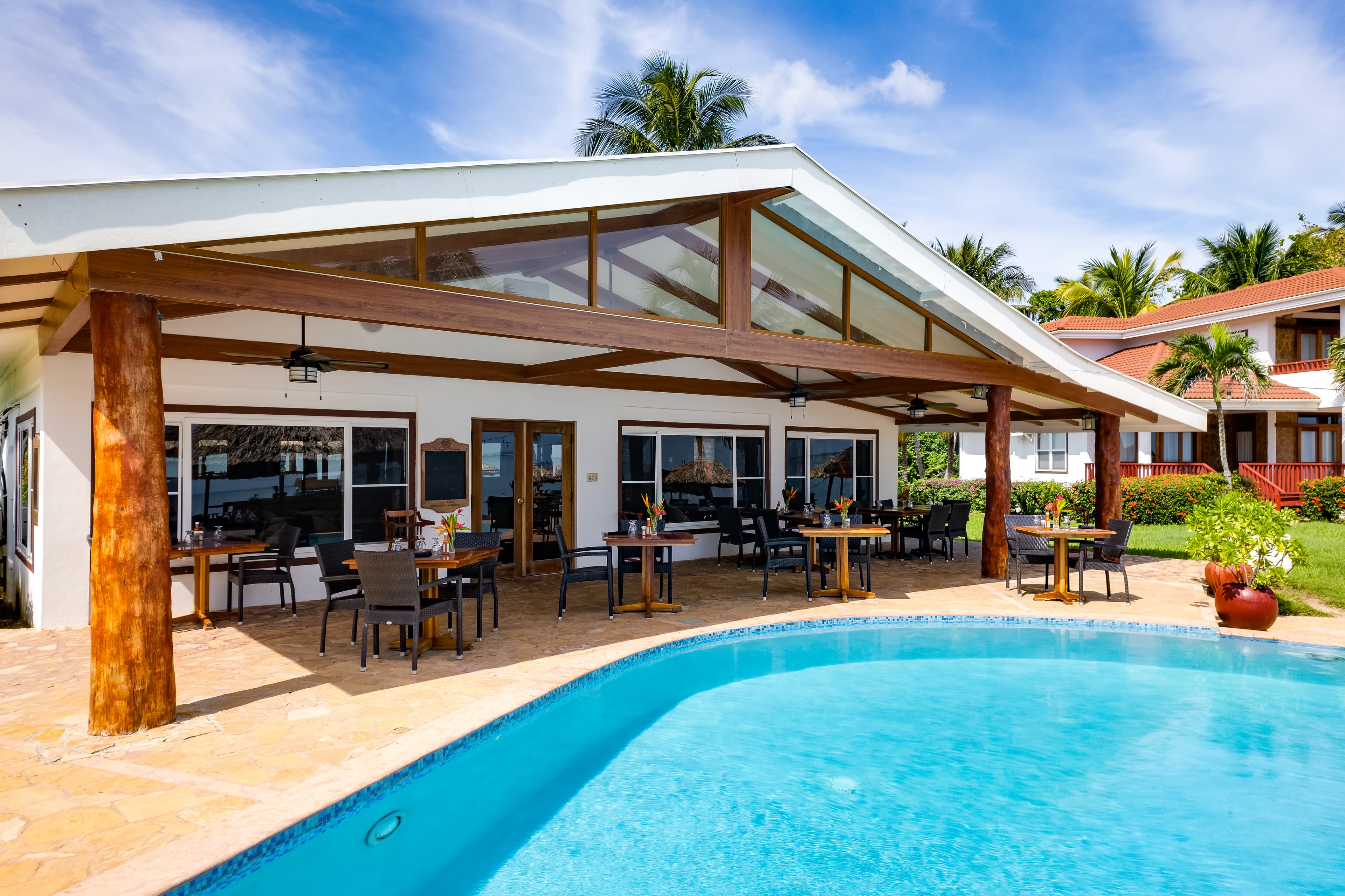 The resort features a swimming pool surrounded by lounge chairs and and bartables and other buildings.