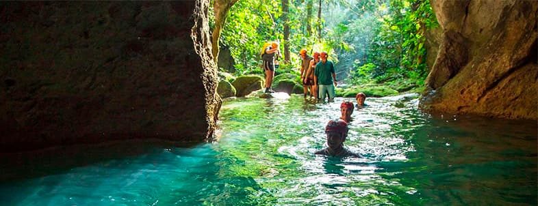 People exploring a lush, tropical cave with clear blue water. People exploring a lush, tropical cave with clear blue water.