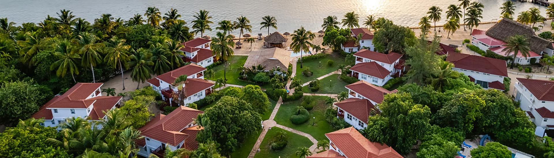Ariel view of property with ocean, red roof villas and accommodation, pathways to the ocean and palm trees and grass.