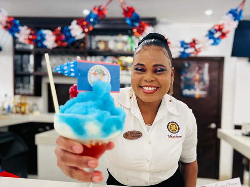 A smiling bartender holds up a colorful dessert with a small flag decoration. A smiling bartender holds up a colorful dessert with a small flag decoration.
