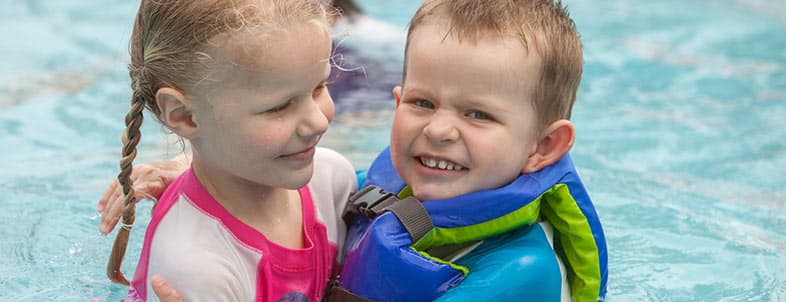 Two children play happily in a swimming pool, with one wearing a colorful life jacket. Two children play happily in a swimming pool, with one wearing a colorful life jacket.