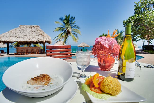 A gourmet meal of fish, rice, and salad is set on a table next to a pool with a scenic ocean view.