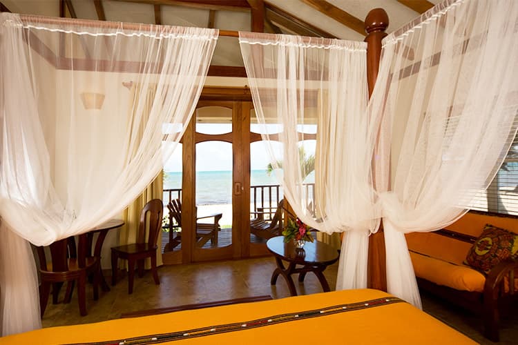 A cozy beachside room with sheer curtains, wooden furniture, and a view of the ocean.