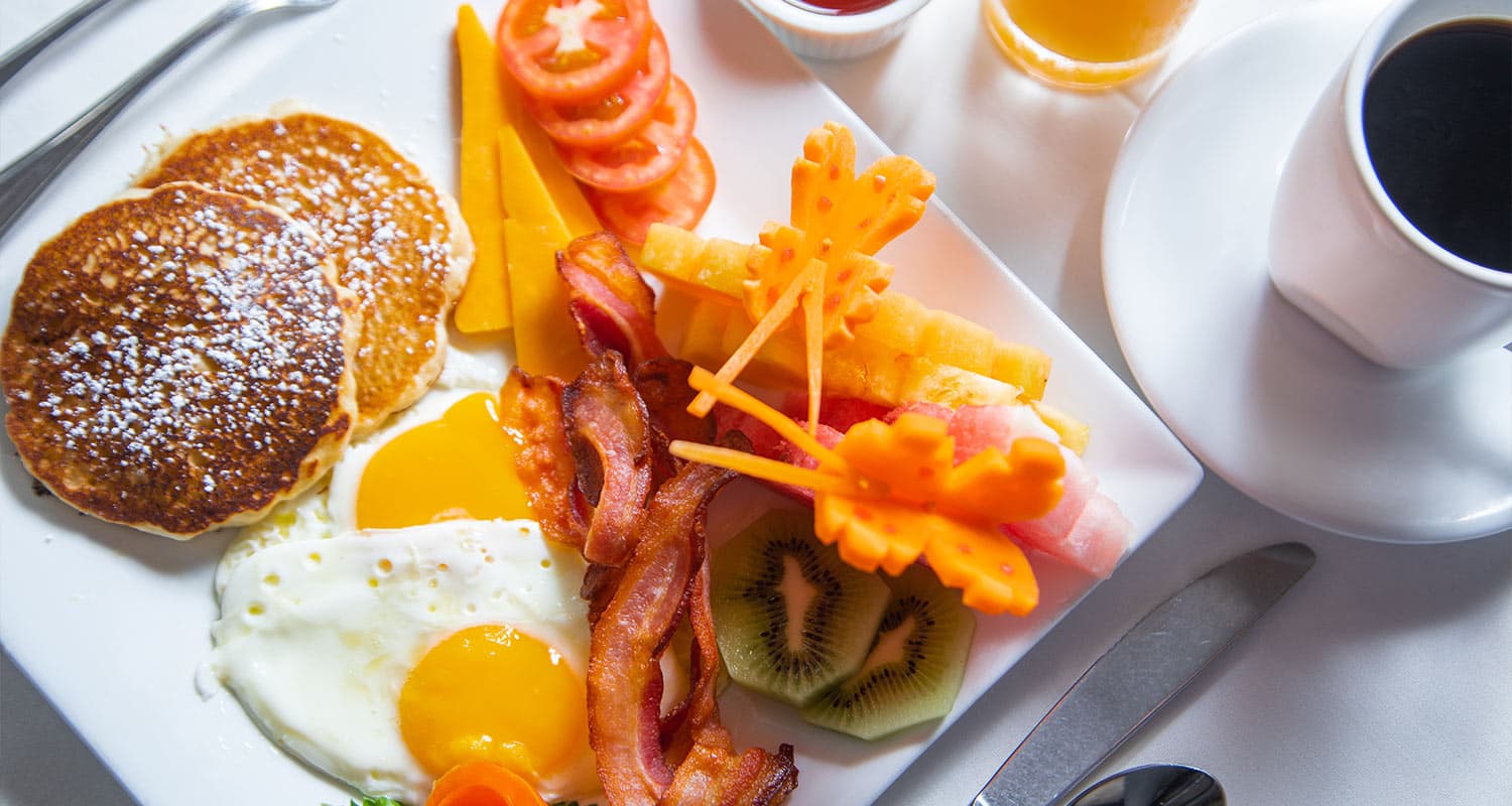 The image shows a delicious-looking breakfast plate. There are pancakes, bacon, eggs, fruit, and cheese. It looks like a hearty and satisfying meal to start the day.