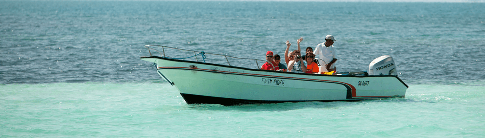 A group of people head out on a boat while the captain mans the tiller.