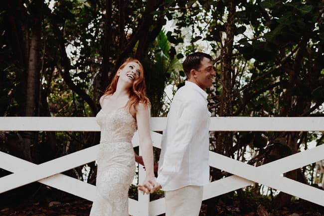 A joyful couple holds hands while standing back to back in a lush outdoor setting.