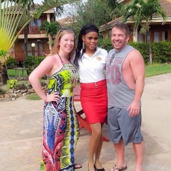 A happy and relaxed couple pose in front of villas with a member of the resort staff.