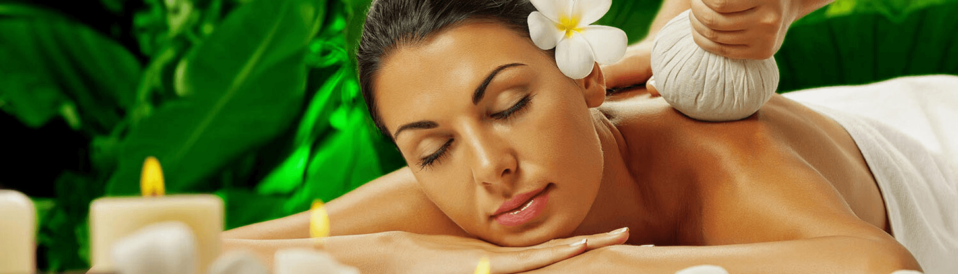 A lovely brunette woman with a flower in her hair receives a spa massage, surrounded by candles.