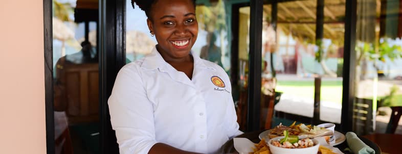 A smiling waitress stands in front of a restaurant holding a tray of food. A smiling waitress stands in front of a restaurant holding a tray of food.