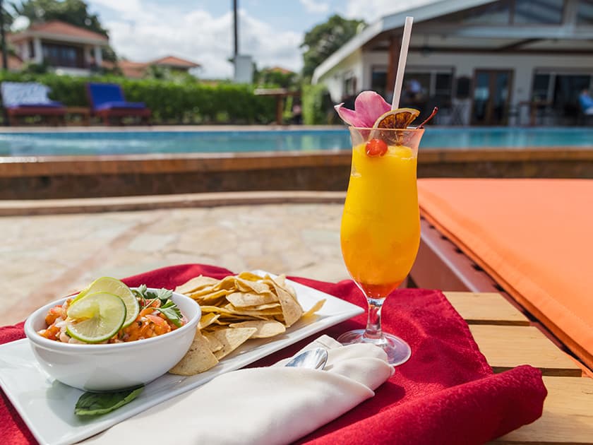 A refreshing tropical drink and a bowl of seafood salad with tortilla chips, set by a poolside.