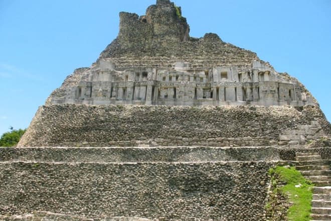 Ancient stone pyramid surrounded by lush greenery under a clear blue sky.
