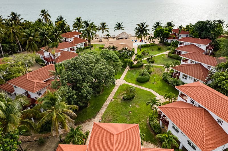 Aerial view of a tropical resort complex with red-roofed buildings surrounded by greenery and palm trees.