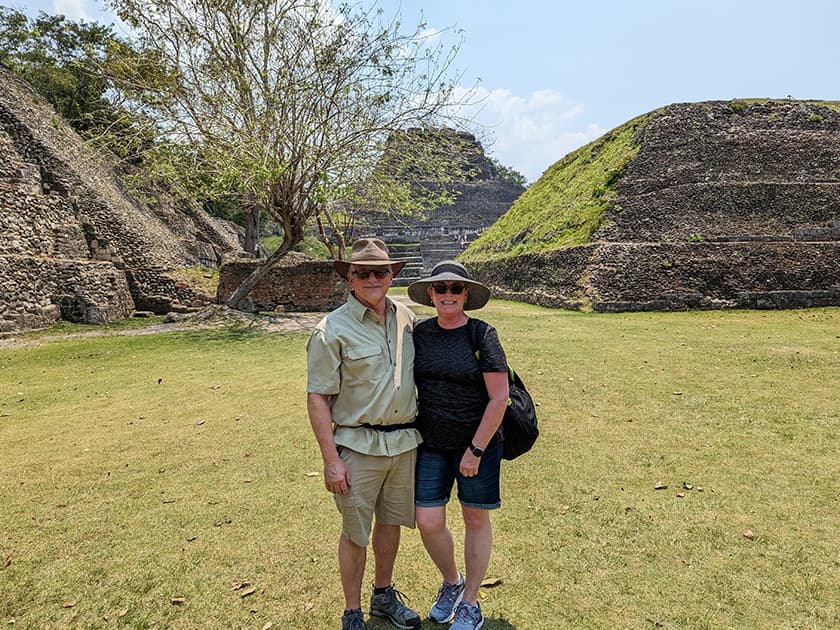 A couple stands together in front of ancient ruins under a clear sky.