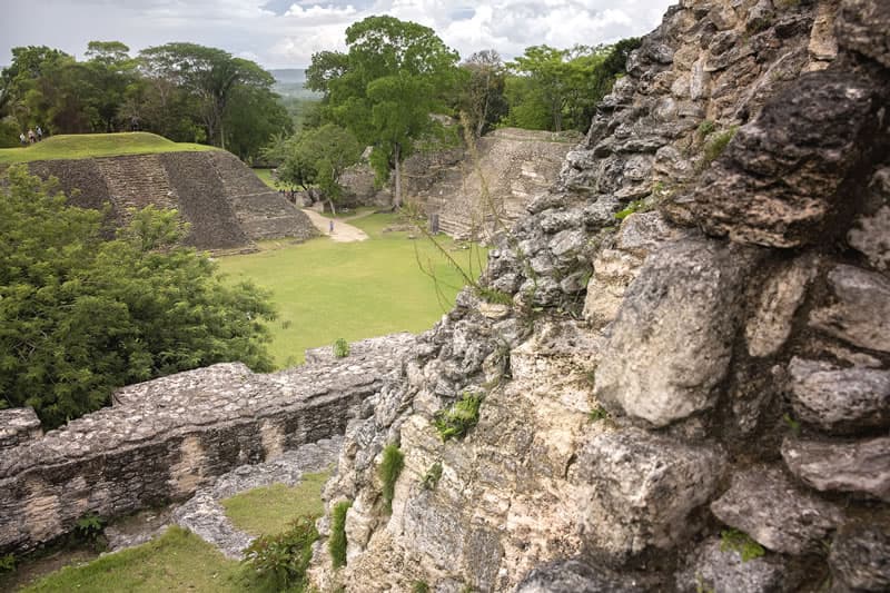 Ruins of ancient structures surrounded by greenery and trees under a cloudy sky.