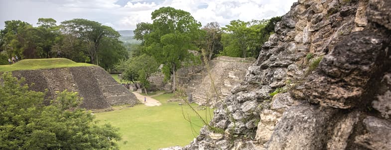 Ancient ruins with stone structures and green trees under a cloudy sky.
