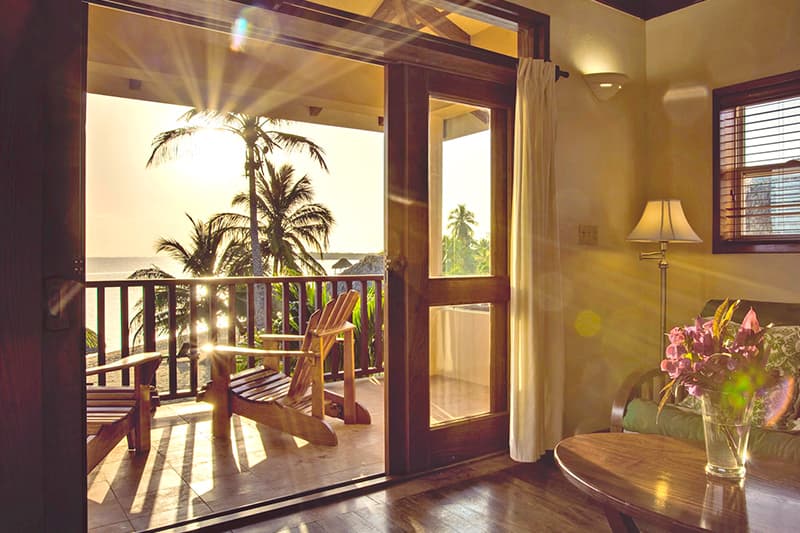 A sunlit room opens to a balcony with palm trees and ocean views. A sunlit room opens to a balcony with palm trees and ocean views.