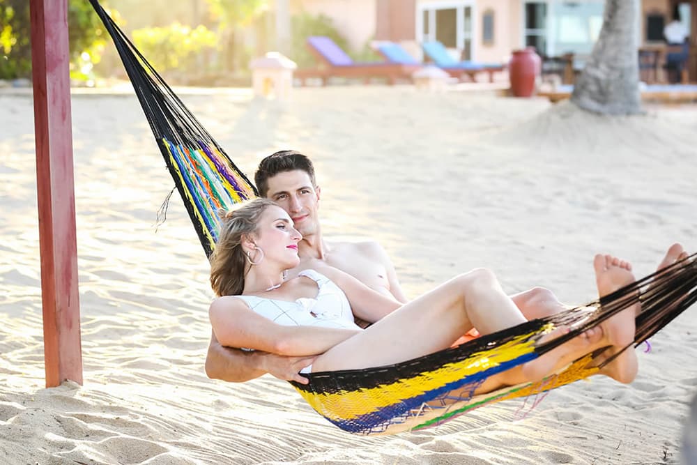 A blonde woman and a dark-haired man rest together in a colorful beach hammock on a sunny breezy day.