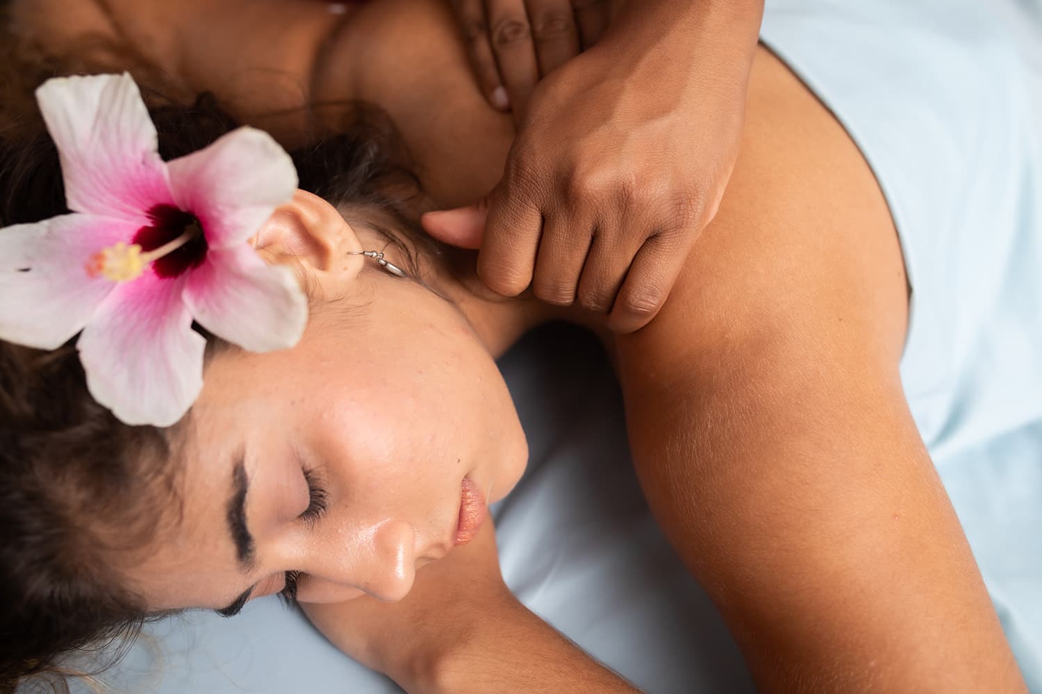 A lovely brunette woman with a flower in her hair receives a spa massage.