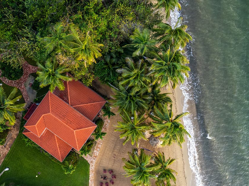 Aerial view of a spacious Belize villa surrounded by palm trees and sandy shoreline.