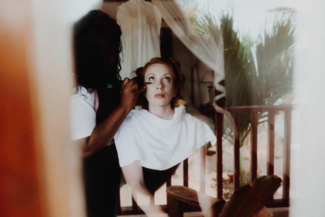 A woman receiving makeup application while seated indoors.