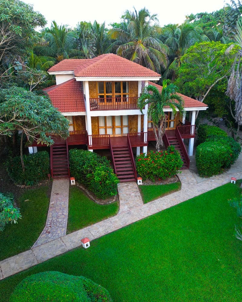 A two-story house surrounded by lush greenery and a stone pathway.