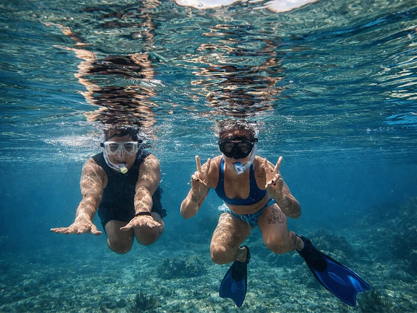 Two figures swimming underwater, wearing snorkel gear and making peace signs. Two figures swimming underwater, wearing snorkel gear and making peace signs.