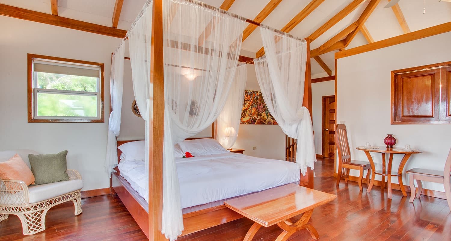 Guest room with 4 poster and white linens, hardwood floors, table and chairs, and white walls.