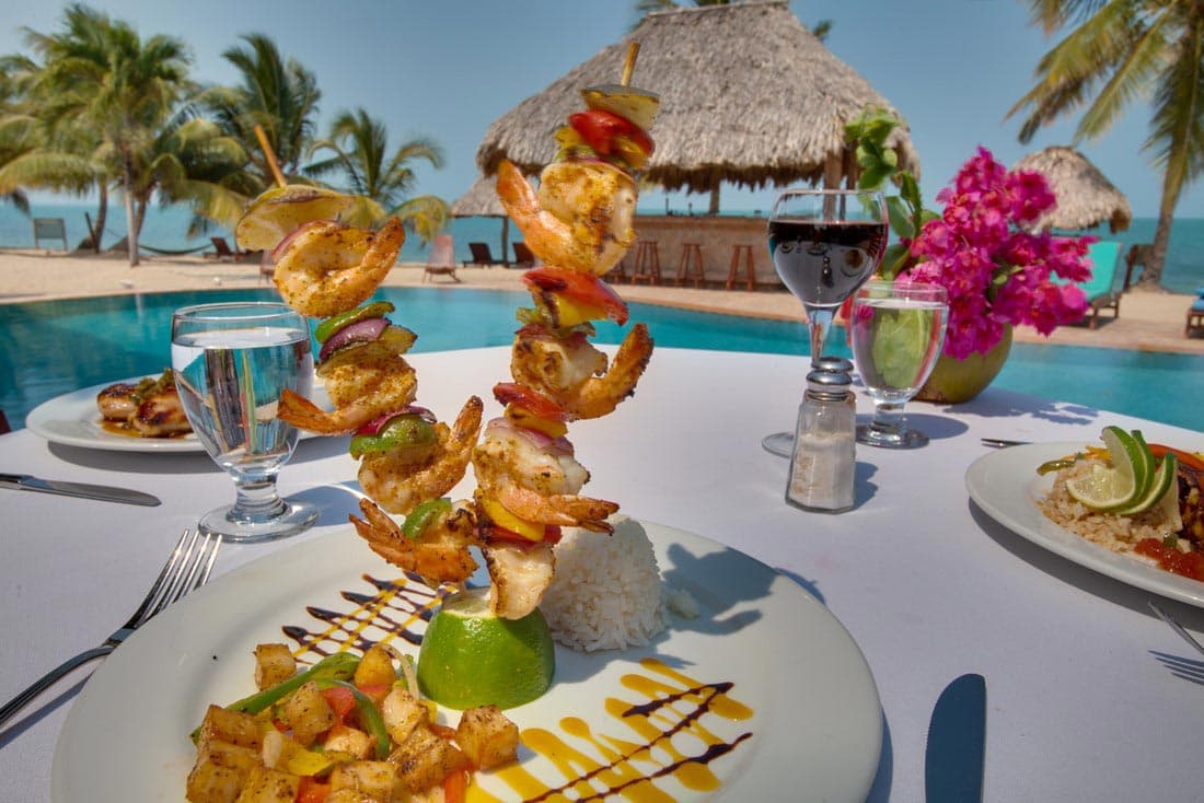 A delicious seafood dish served on a white plate at a beachfront restaurant. The dish features grilled shrimp on a skewer, accompanied by rice, vegetables, and a lime wedge.