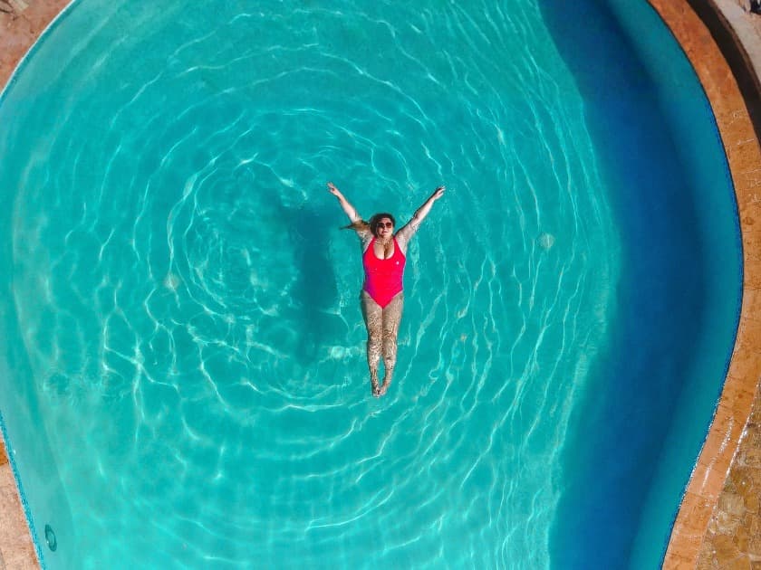 A person in a red swimsuit floats with arms outstretched in a clear blue swimming pool.