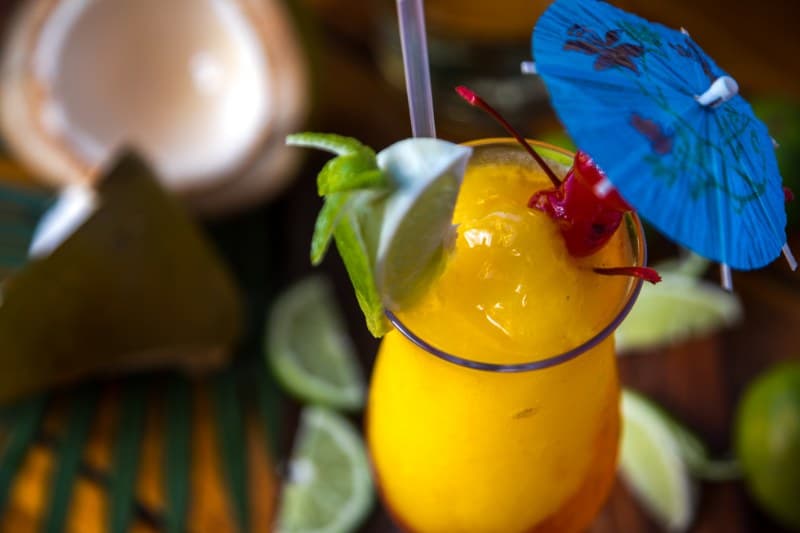 A vibrant tropical cocktail garnished with a cherry, lime, and an umbrella, surrounded by fresh fruit and greenery. A vibrant tropical cocktail garnished with a cherry, lime, and an umbrella, surrounded by fresh fruit and greenery.