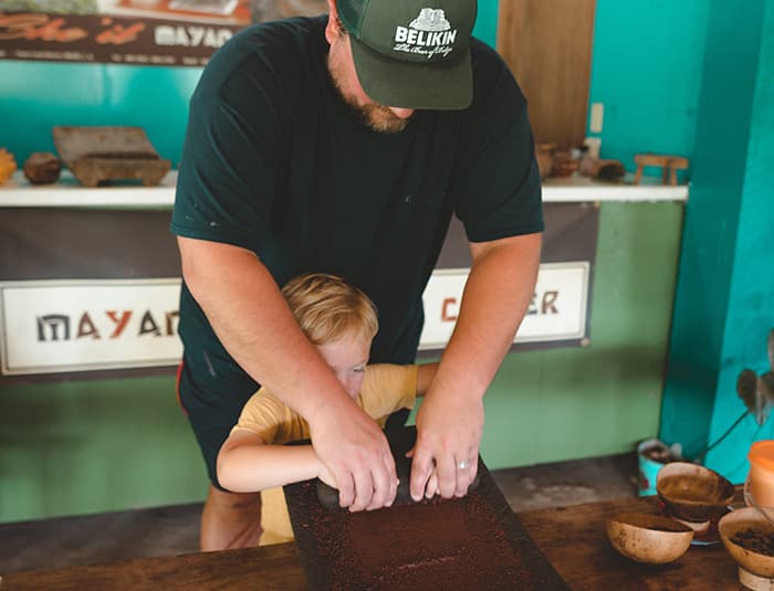 A man helps his little son grind cacao beans.