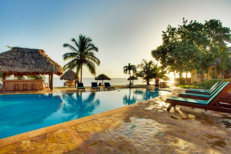Tropical poolside scene at sunset, featuring lounge chairs and palm trees.
