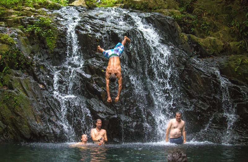 A person dives into a natural pool from a rocky ledge while others swim nearby.