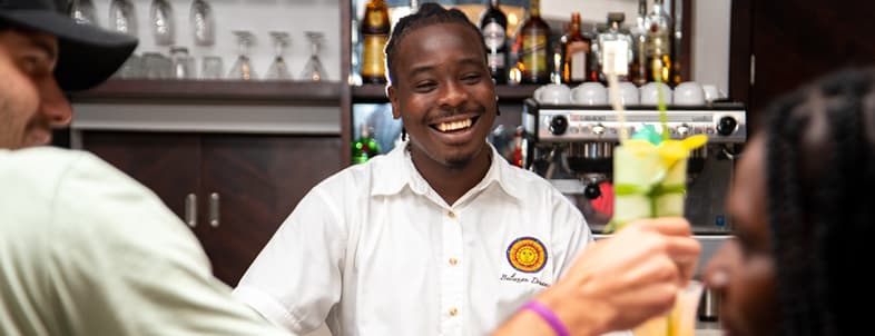 A smiling bartender interacts with patrons at a lively bar.